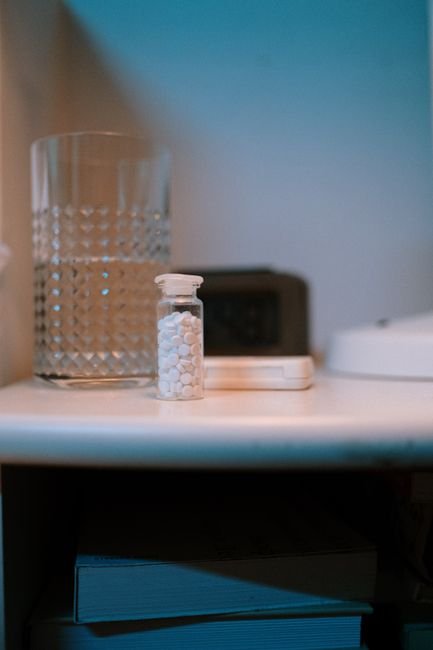 Small pill bottle beside a glass of water on a bedside table