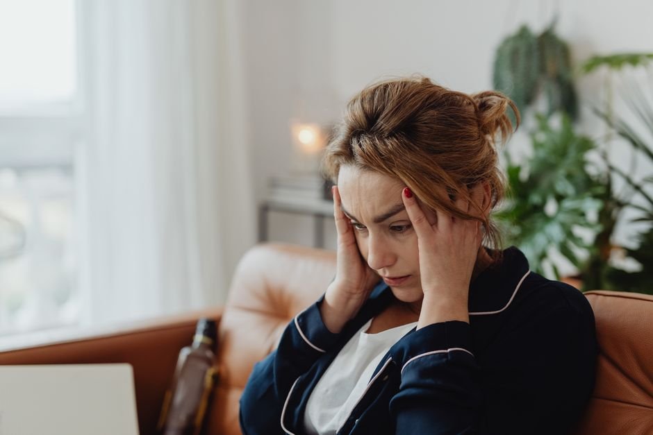 A person sitting on a couch holding their temples, looking troubled
