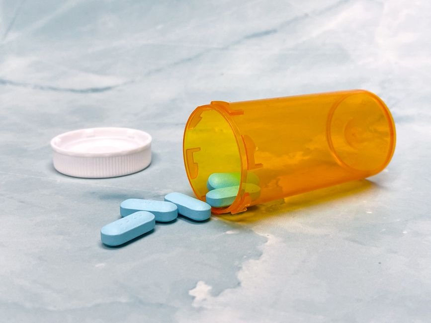 An open prescription pill bottle with capsules spilled next to it