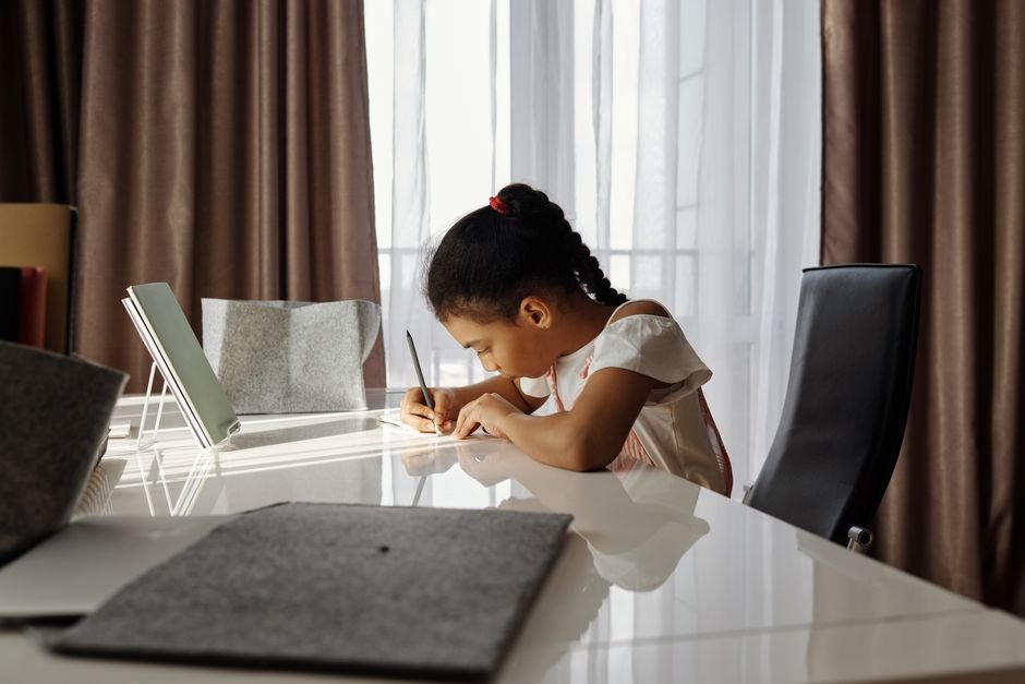 A child focused on writing at a desk near a window