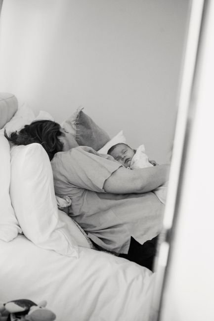 Mother resting in bed while holding her sleeping newborn