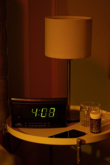 Digital alarm clock reading 4:08 next to a pill bottle and glass of water on a nightstand