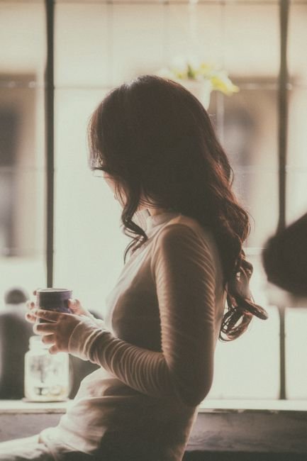 Woman sitting quietly by a window in soft morning light, holding a warm drink