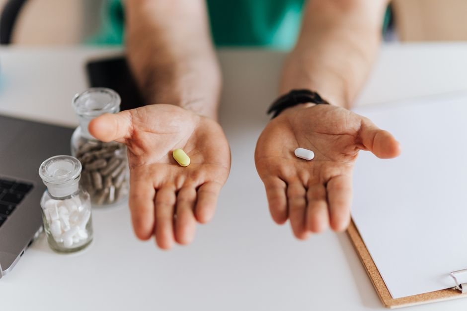 Two open hands, each holding a different single pill, side by side