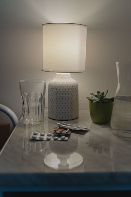 Blister pack of pills and a water glass on a bedside table lit by a lamp