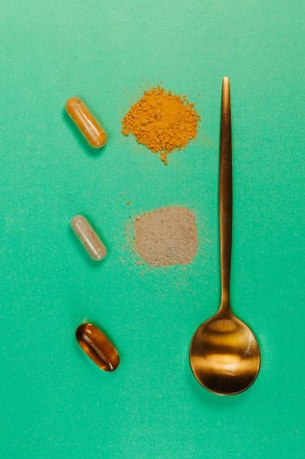 Herbal capsules and powder measured with a spoon on a green surface