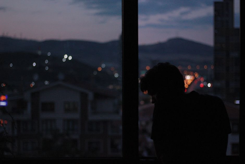 Silhouette of a person standing by a window at night overlooking city lights