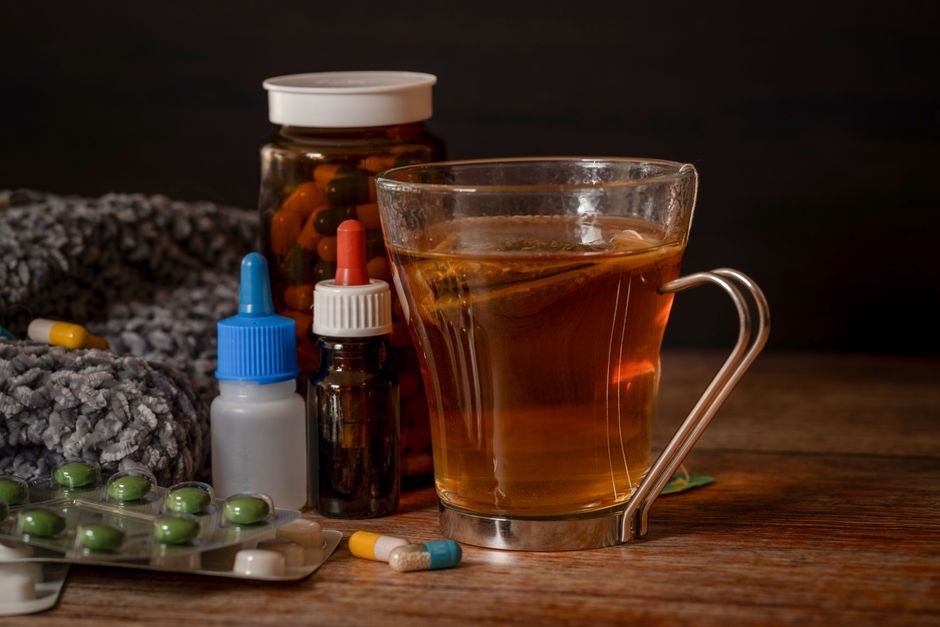 Cold and flu remedies including capsules and a warm cup of tea on a nightstand