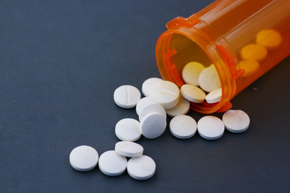 White pills spilling out of an orange prescription bottle onto a dark surface